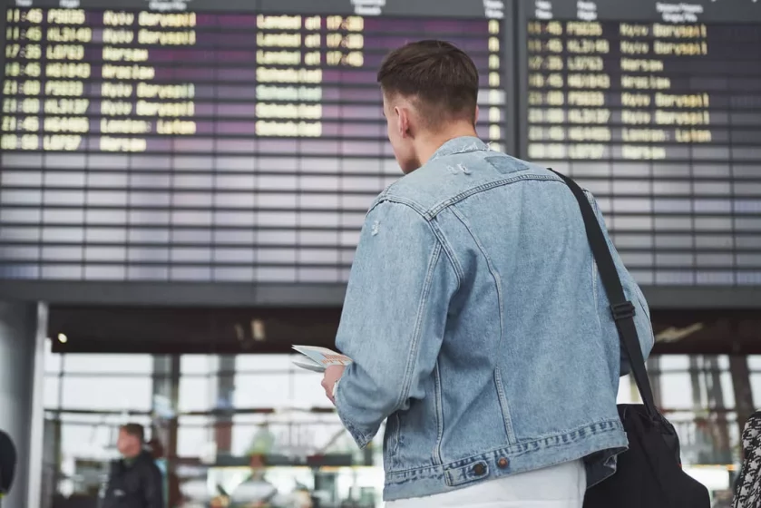 Jovem conferindo voo no painel do aeroporto - Dicas para primeira viagem internacional