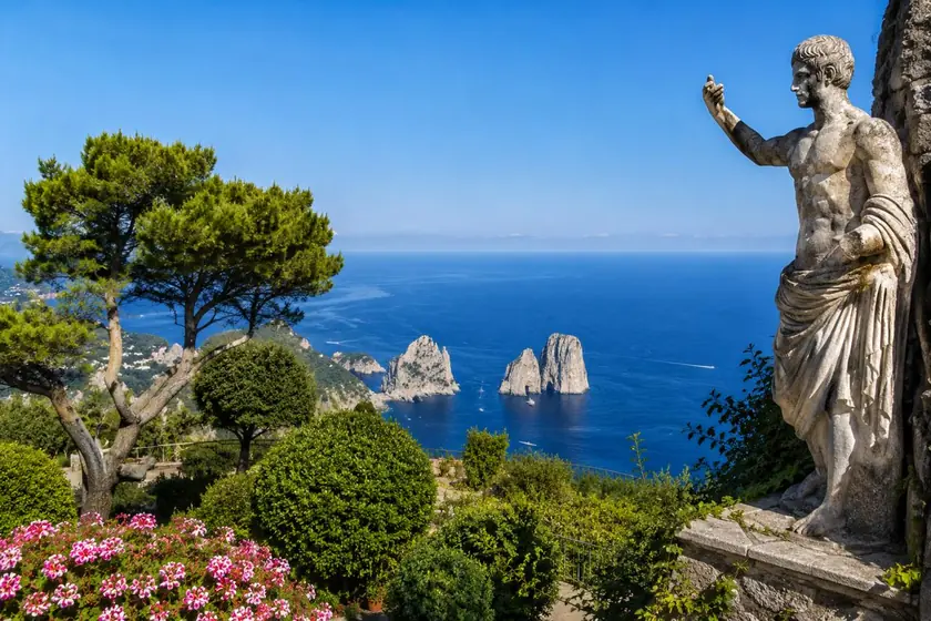 Vista dos Faraglioni de Capri a partir dos Jardins de Augusto, com estátua e vegetação.